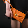 Orange Leather Purse Held by Person in Black Dress on Black Background